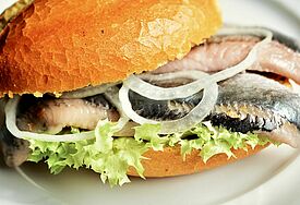 Ein Matjes-Fischbrötchen mit Salat und Zwiebeln auf einem weißen Teller