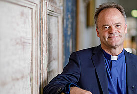 Bischof Tilman Jeremias im blauen Anzug in einer Kirchenbank sitzend.