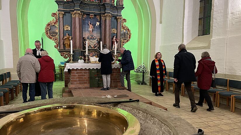 Ein Altarraum in einer alten Dorfkirche mit Menschen, die zum Segnen kommen.