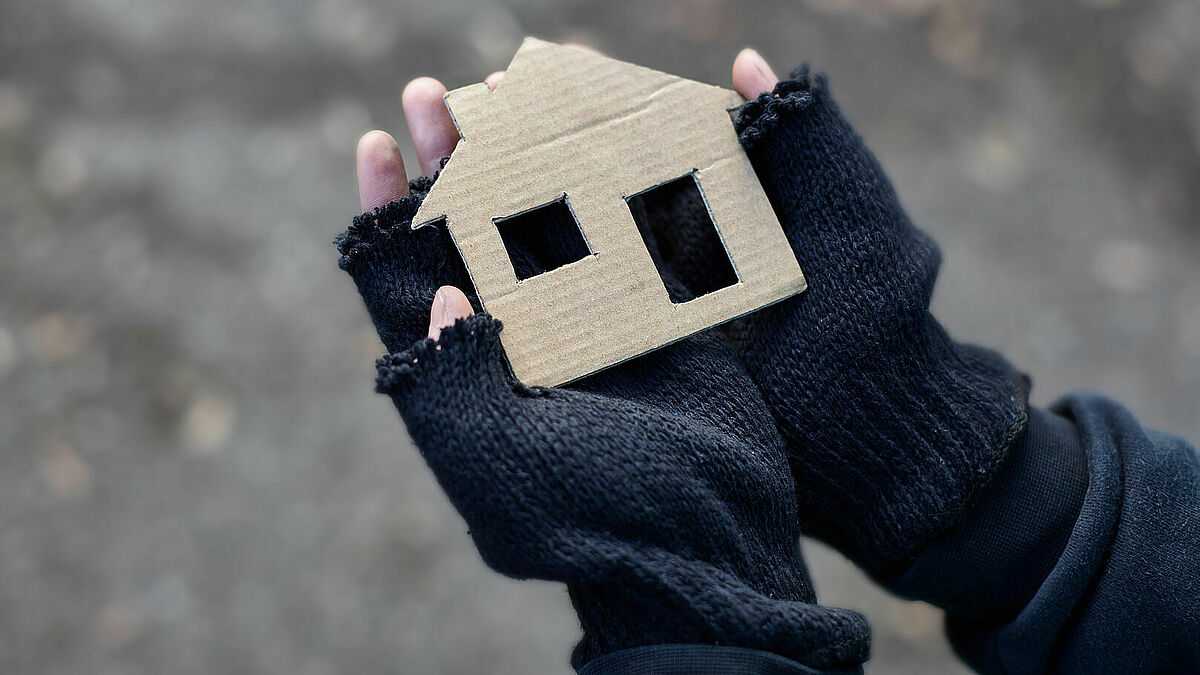Obdachloser Junge hält ein Karton-Haus in den Händen