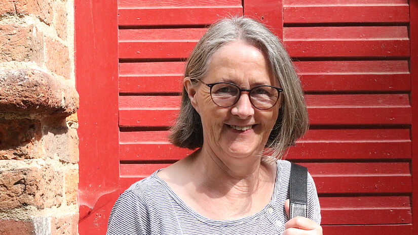 Anngret Ohlendorf Anngret Ohlendorf steht vor der roten Holztür der Dorfkirche auf der Insel Poel