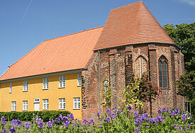 Das Gebäude des Barther Bibelzentrums leuchtet gelb in der Sommersonne, im Vordergrund blühen lila Blumen