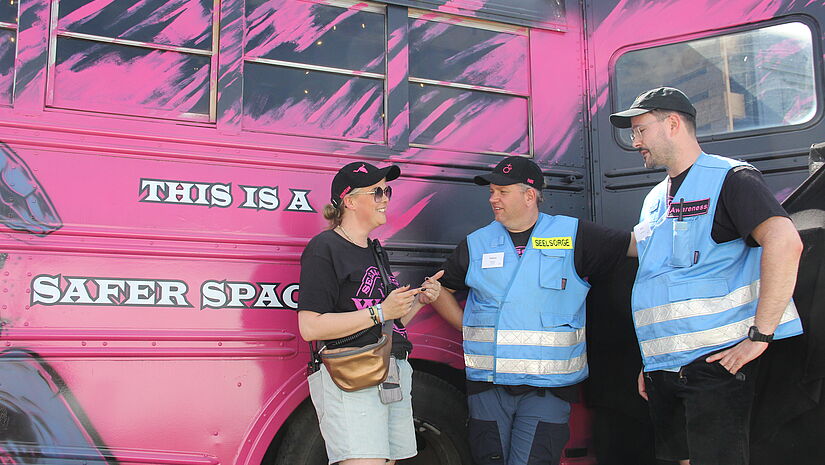 Zwei Männer und eine Frau vor einem pinkfarbenen Bus