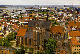 Luftaufnahme der St.-Georgen-Kirche in Wismar. Im Hintergrund ist der Hafen und die Ostsee zu sehen.