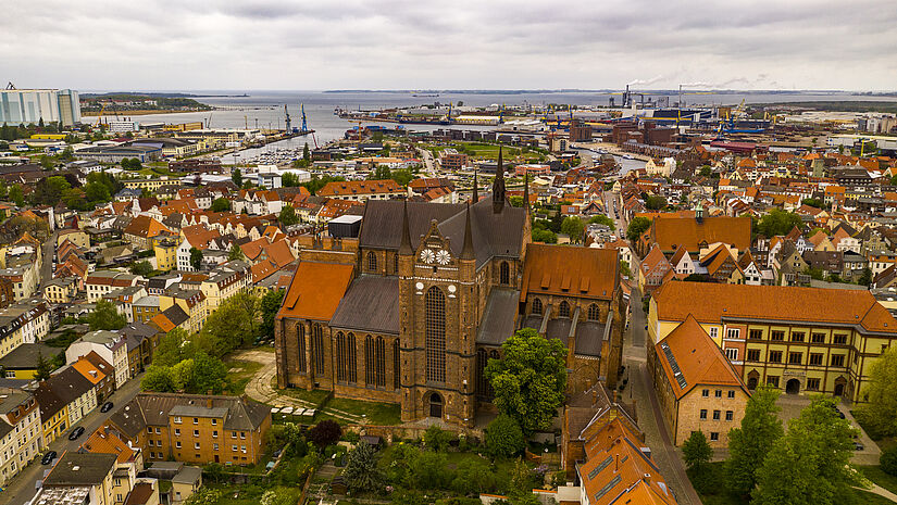 Luftaufnahme der St.-Georgen-Kirche in Wismar. Im Hintergrund ist der Hafen und die Ostsee zu sehen.