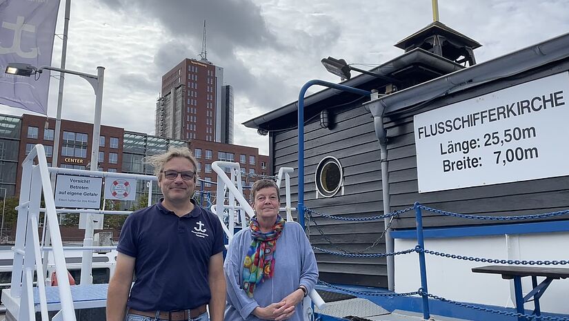 Diakon Mark Möller und Ehrenamtliche Gislea Bruns vor dem Eingang zur Flussschifferkirche – Deutschlands einzige schwimmende Kirche. 