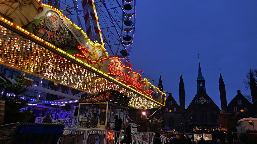 Die Lichter eines Riesenrads leuchten hell in der Dunkelheit auf dem maritimen Weihnachtsmarkt in Lübeck.