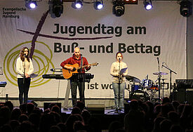 Junge Menschen musizieren auf der Bühne vor Publikum, im Hintergrund das Banner des Jugendtags.