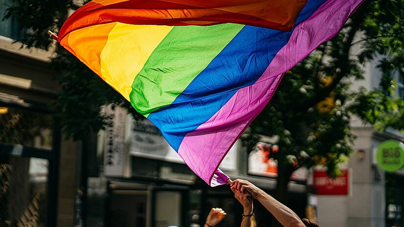 Die Regenbogenflagge symbolisiert Vielfalt. Alle Menschen sind eingeladen, sie als Zeichen der Solidarität mit der LGBTQ-Community zu tragen. Hand, die eine Regenbogenflagge auf der Straße schwenkt