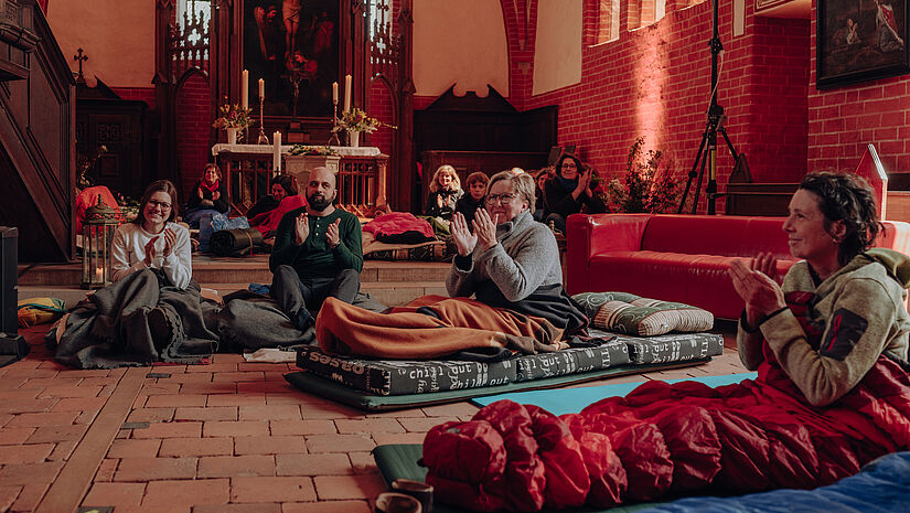 Menschen liegen und sitzen auf Matratzen im Kirchengebäude und klatschen