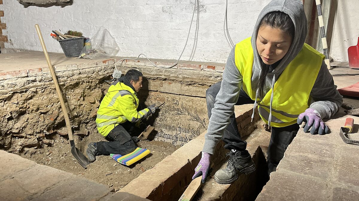 Thai Nguy (l.) und Joana Laura Noack vom archäologischen Team der Stadt Lübeck legen die Wandmalereien in einer historischen Gruft frei.