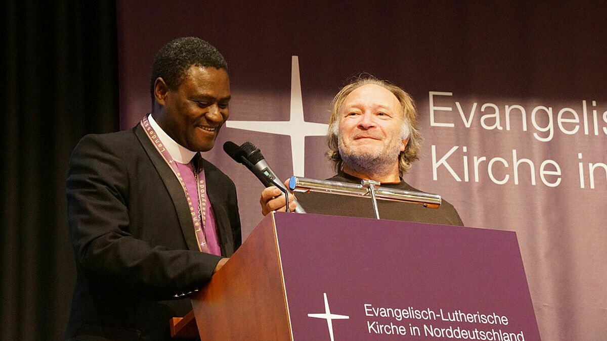 Der Bischof der Evangelisch-Lutherischen Kirche in Tansania (ELCT), Andrew Gulle (l.), überbrachte den Synodalen seinen Dank. Pastor Rolf Martin aus Lübeck übersetzte
