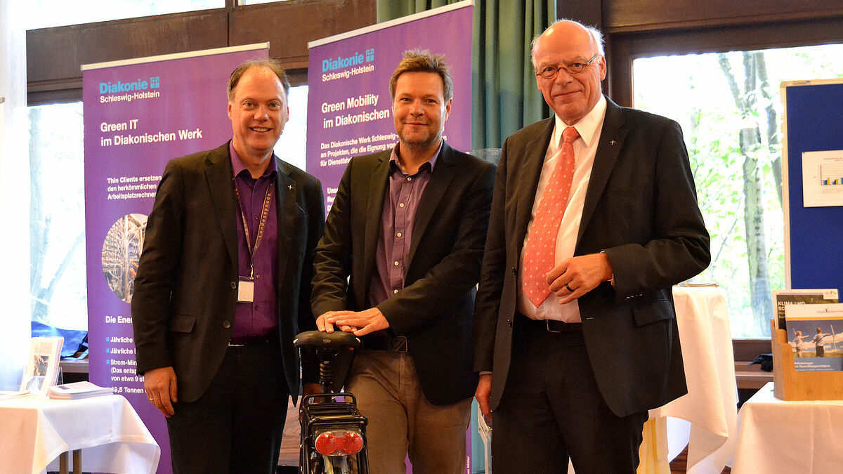 V.l.n.r.: Dr. Andreas Tietze (Synoden-Präses), Dr. Robert Habeck (Umweltminister des Landes Schleswig-Holstein) und Gerhard Ulrich (Landesbischof der Nordkirche) mit dem E-Bike der "Kirche für Klima". Habeck sprach ein Grußwort auf der Klima-Synode.