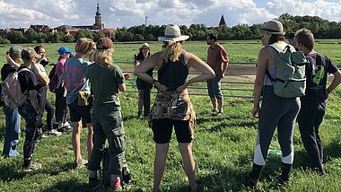 Eine Gruppe von jungen Menschen steht auf einer Wiese, im Hintergrund Kirchtürme