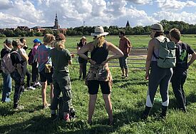 Eine Gruppe von jungen Menschen steht auf einer Wiese, im Hintergrund Kirchtürme