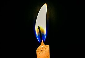 Eine Kerze brennt mit blau-gelber Flamme vor schwarzem Hintergrund.