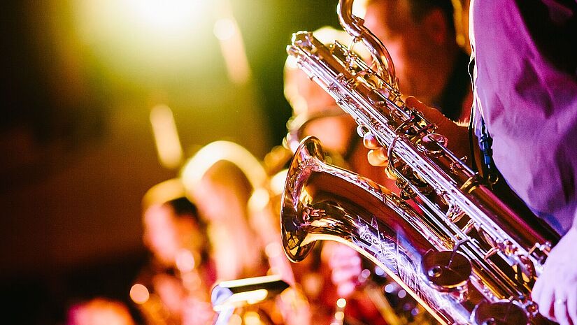 Band Im Vordergrund ein Saxophon, im Hintergrund unscharf weitere Bandmitglieder, warmes Licht