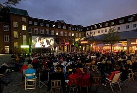 Es ist dunkel, viele Menschen sitzen vor einer illuminierten Leinwand