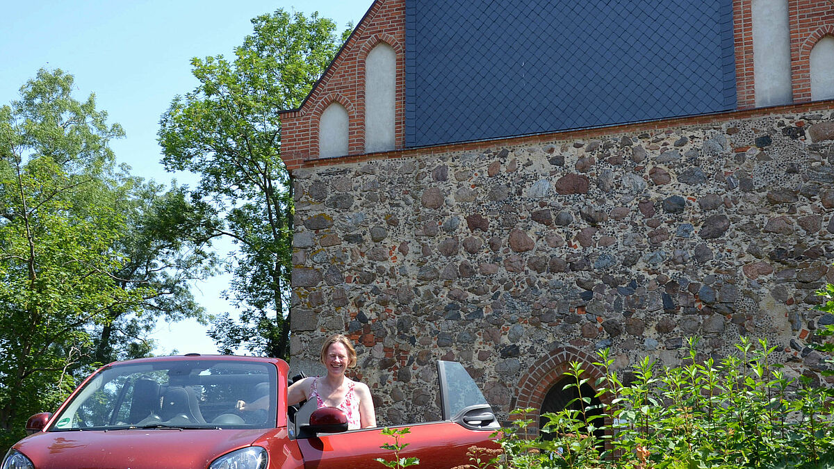 Pastorin Verena Häggberg mit dem e-Auto vor der Kirche Vipperow