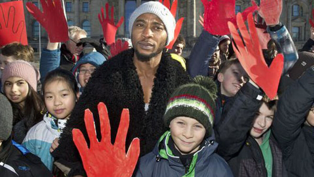 Schüler aus Berlin demonstrieren am Montag (10.02.2014) zusammen mit dem ehemaligen Kindersoldaten Michael Davies (M.) aus Sierra Leone zum "Red Hand Day" am 12. Februar vor dem Reichstag in Berlin. 