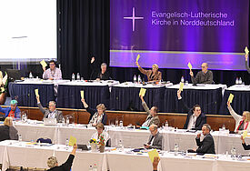 Abstimmung der Landessynode: Die Synodalen halten gelbe Stimmzettel nach oben.