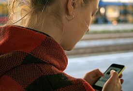 Mädchen steht am Bahnhof und blickt auf ihr Telefon.