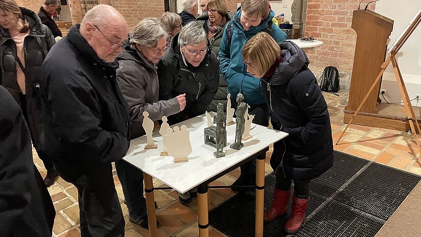 eine Gruppe von Menschen rund um einen Tisch mit Krippenfiguren
