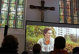 Leinwand mit Film in der Kirche, davor die Zuschauer