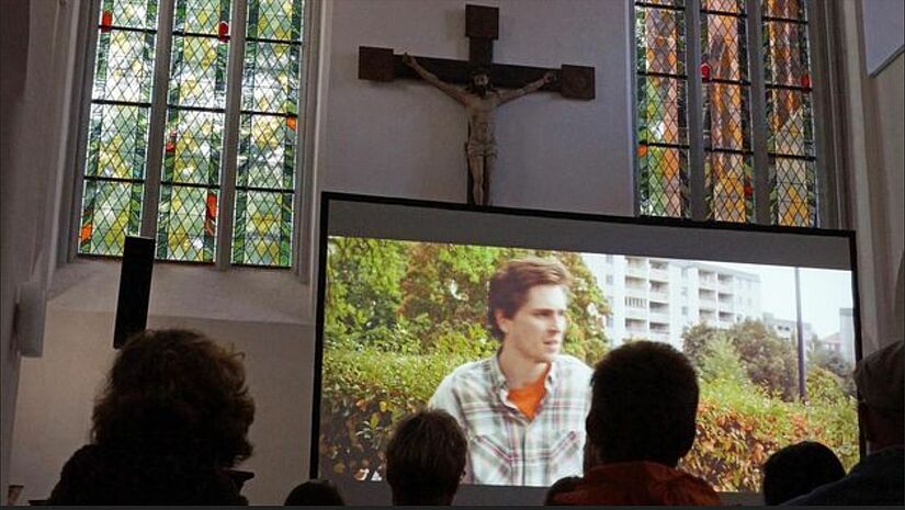 Leinwand mit Film in der Kirche, davor die Zuschauer