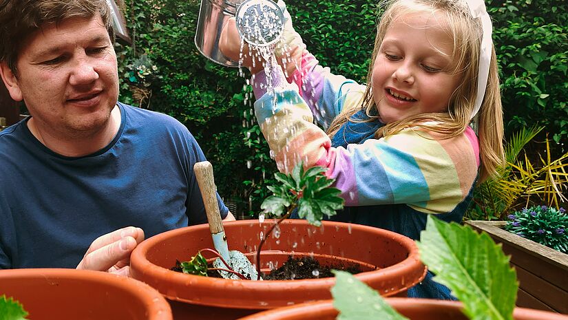 Kind und Erwachsener gießen Pflanzen