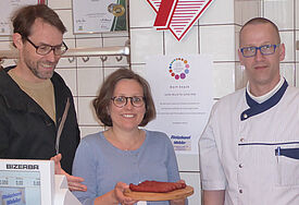 Karen Kult, Leiterin des Netzwerks der evangelischen Johannes-Gemeinde in Hamburg-Rissen, präsentiert den "Dorf-Snack" zusammen mit Fleischermeister Jürgen Wohler (r.) und dem Rissener Pastor Steffen Kühnelt.