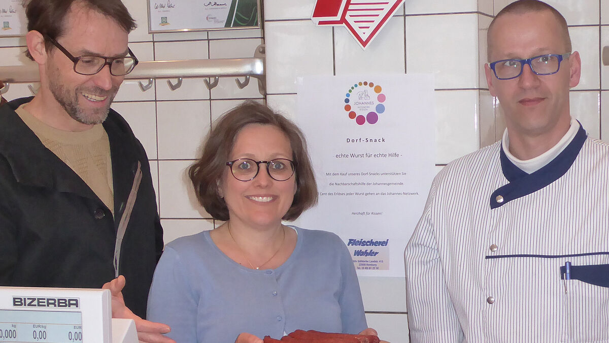 Karen Kult, Leiterin des Netzwerks der evangelischen Johannes-Gemeinde in Hamburg-Rissen, präsentiert den "Dorf-Snack". Damit soll das soziale Leben im Stadtteil unterstützt werden. Fleischermeister Jürgen Wohler (rechts) hat den "Dorf-Snack" hergestellt. Links der Rissener Pastor Steffen Kühnelt. 