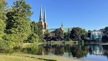 Der Lübecker Dom mit zwei Türmen im Morgenlicht, im Vordergrund eine Wasserfläche.