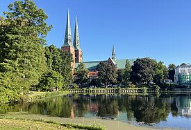Der Lübecker Dom mit zwei Türmen im Morgenlicht, im Vordergrund eine Wasserfläche.