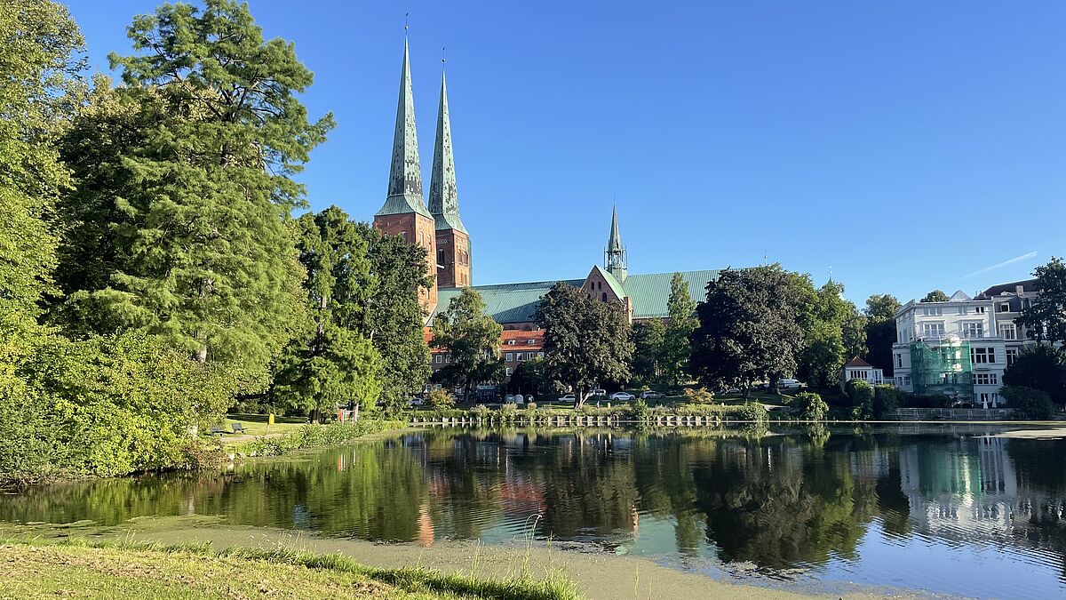 Als ich Lübeck auf dem Jakobsweg verlasse, spiegeln sich die Türme des Lübecker Domes in der frühen Morgensonne auf der spiegelblanken Wasseroberfläche des Mühlenteiches in Lübeck. 