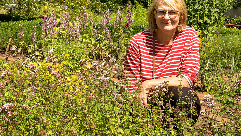 Elke Lenschow umgeben von Würz- und Heilkräutern: Oregano wächst im Vordergrund, dahinter sprießen Muskateller Salbei, Alant und Eibisch. Bei den Führungen durch den Klostergarten erklärt die Gartenbauingenieurin ihren Gästen die heilende Wirkung  und mythologische Bedeutung der Pflanzen.