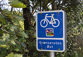 Ein blaues Verkehrsschild mit einem Fahrrad, das eine Route an der dänischen Grenze ausweist