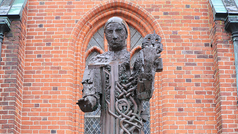 Eine Bronzefigur des Erzbischofs Ansgar vor einer Kirchenwand aus Backstein