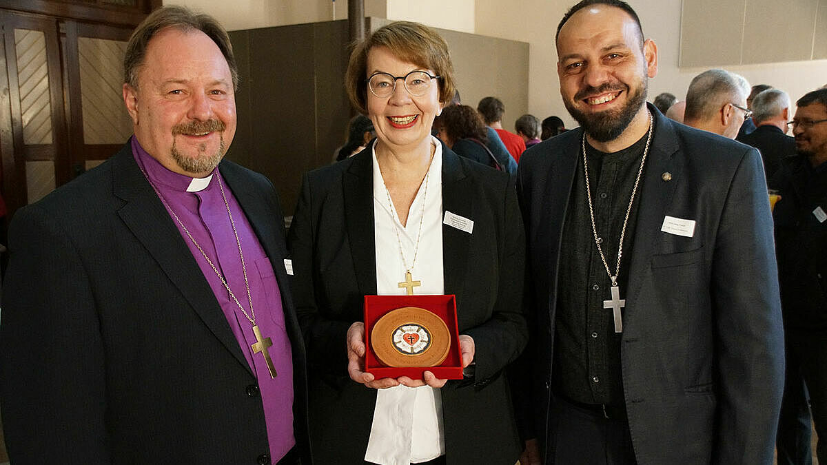 Landesbischöfin Kühnbaum-Schmidt freute sich über das Gastgeschenk von Bischof Dezsö Zoltán Adorjáni (l.) und Oberkirchenrat Dekan Attila Fehér von der Evangelisch-Lutherischen Kirche in Rumänien: eine Keramik-Plakette mit Lutherrose und Namenszügen der Partnerkirchen