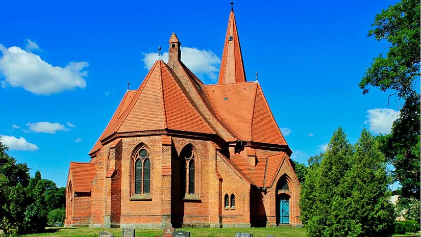 Backsteinkirche, gotiscshe Fenster, Ansicht von hinten, drumherum Rasen, blauer Himmel