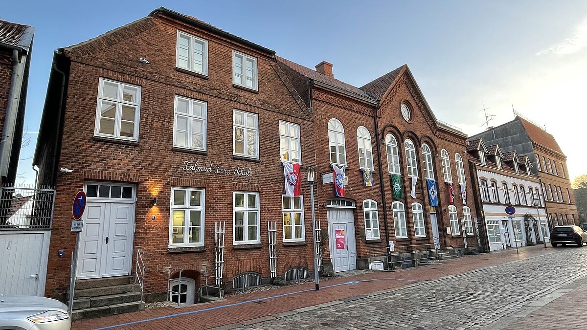 Die Backsteinfassaden der ehemaligen Talmud-Tora-Schule und der früheren Synagoge fügen sich in den Straßenzug ein und wirken wie Wohnhäuser - nicht ohne Absicht. Die bunten Flaggen gehören zu der Ausstellung „Superjuden. Jüdische Identität im Fußballstadion“.  