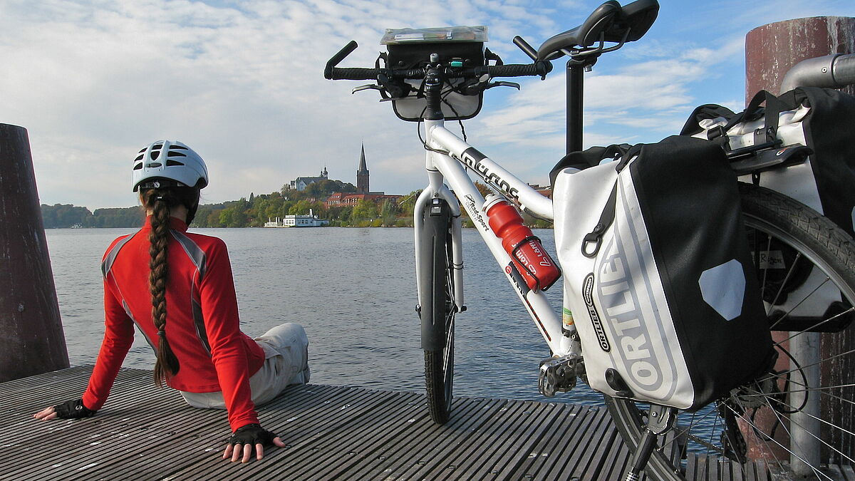 Öfter mal aufs Fahrrad umsteigen, so gelingt umweltfreundliche und nachhaltige Mobilität. Hier: Eine Pilger-Pause mit Blick über den Plöner See auf die Nikolaikirche.