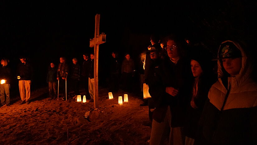 Rund um ein großes Holzkreuz am Strand haben sich teilnehmende Jugendliche in der Dunk.elheit zur Andacht versammelt