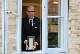 Bischof Gothart Magaard stellt ein Licht ins geöffnete Fenster.
