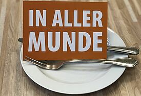 Postkarte, auf der "In aller Munde" steht, steht auf einem weißen Teller mit Besteck
