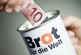 Hand die einen Schein in eine Brot-für-Welt-Spendendose steckt
