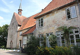 Blick auf eine alte Kirche mit einem kleinen Rundportal und einem repräsentativen Gebäude im Vordergrund.