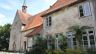Blick auf eine alte Kirche mit einem kleinen Rundportal und einem repräsentativen Gebäude im Vordergrund.