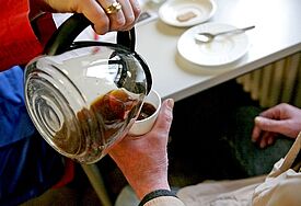 Eine ehrenamtliche Mitarbeiterin schenkt in einer Bahnhofsmission einem Gast noch einen Kaffee nach.