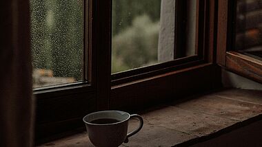 Eine Tasse Kaffee auf einem Fensterbrett, auf der Scheibe Regentropfen
